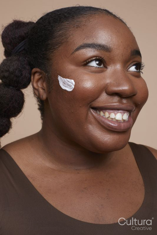 Studio shot of smiling young woman applying face cream
