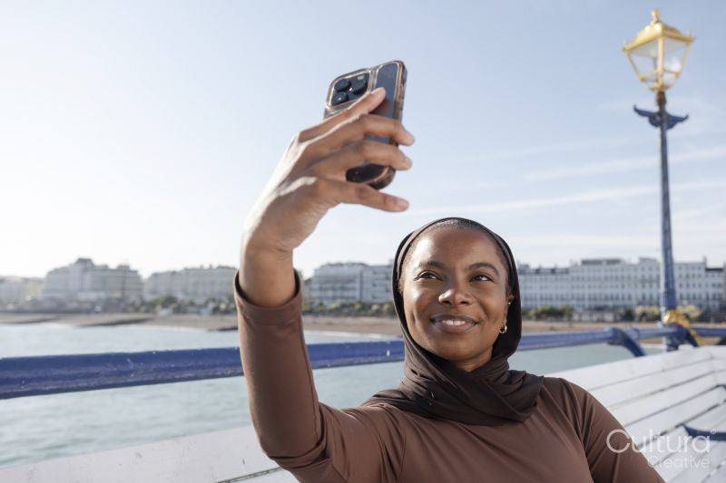 Muslim woman taking selfie with sea view on sunny day