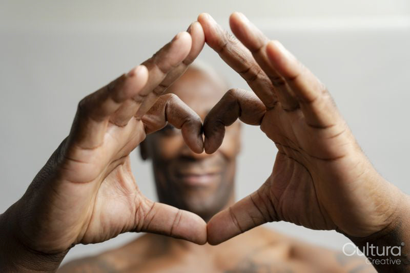 Portrait of man making heart gesture in front of head against gray background