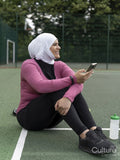 Sutton,Woman in headscarf sitting on tennis court,holding smart phone