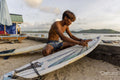 Indonesia, Lombok, Surfer preparing surfboard on beach at sunset
