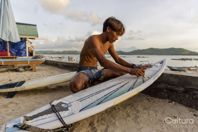 Indonesia, Lombok, Surfer preparing surfboard on beach at sunset
