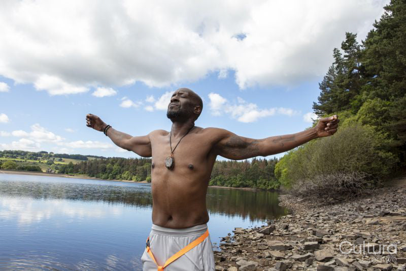Shirtless man with arms outstretched on rocky lakeshore, Yorkshire, UK