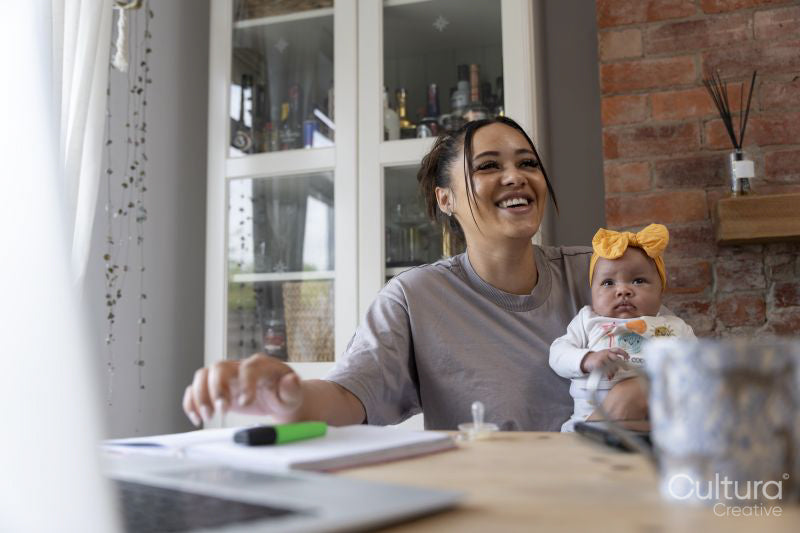 Smiling mother holding baby girl while studying at home