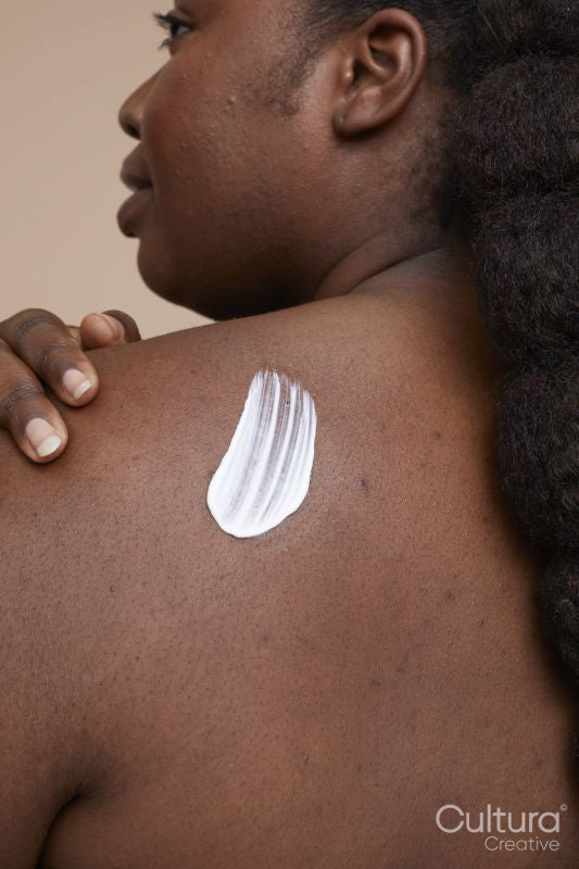 Studio shot of young woman applying moisturizer on back