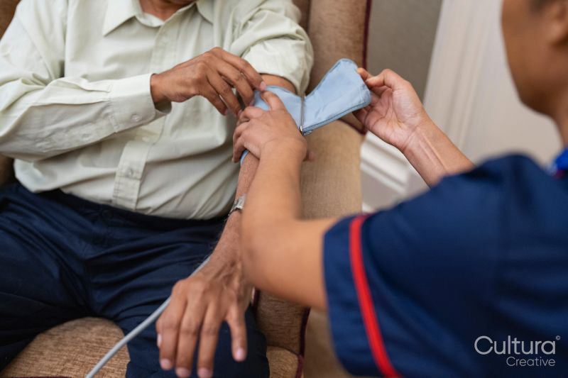 Nursing assistant adjusting blood pressure gauge on senior mans arm in nursing home