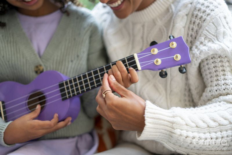 Close-up of mother teaching daughter playing ukulele