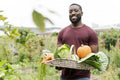 Portrait of smiling man holding basket with fresh vegetables in urban garden