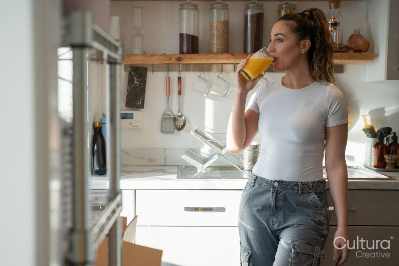 Woman in kitchen, drinking orange juice