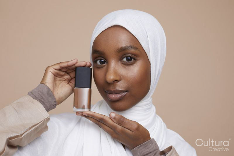 Studio portrait of young woman in white hijab holding foundation bottle