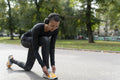 Portrait of woman in sports clothing and headphones tying shoe in park