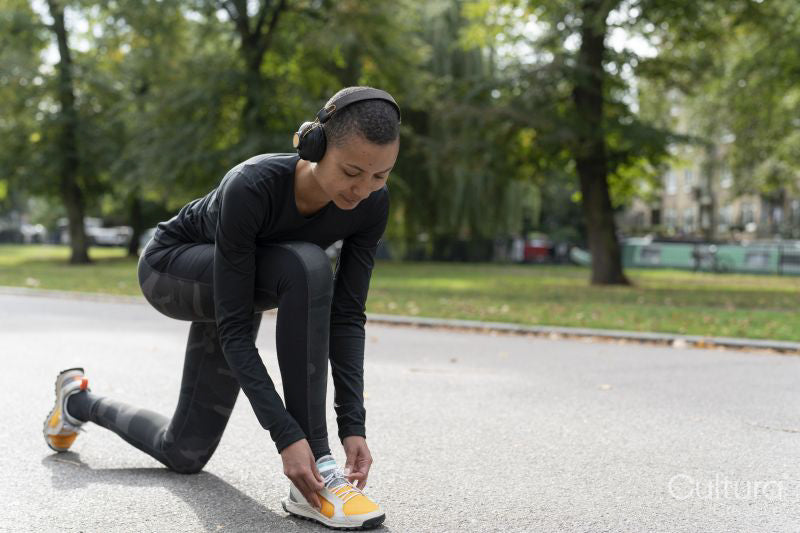 Portrait of woman in sports clothing and headphones tying shoe in park