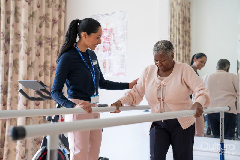 Smiling female therapist assisting senior woman walking on bars