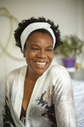 Smiling woman wearing white headband and bathrobe sitting on bed