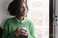Smiling woman holding cup of coffee while looking through window