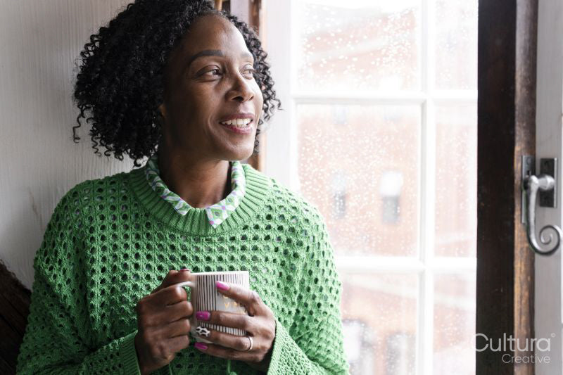 Smiling woman holding cup of coffee while looking through window