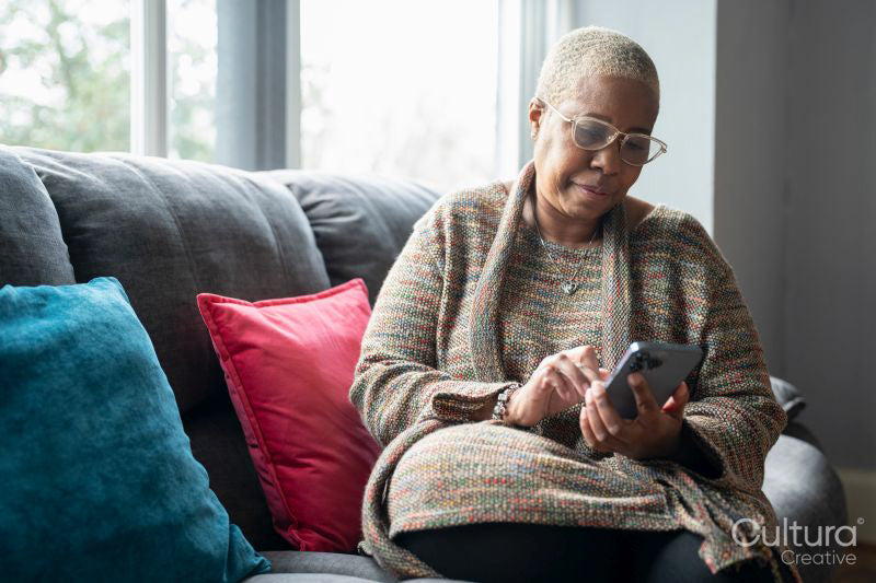 Mature woman sitting in living room with her smart phone