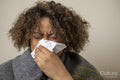 Woman wrapped in blanket blowing nose