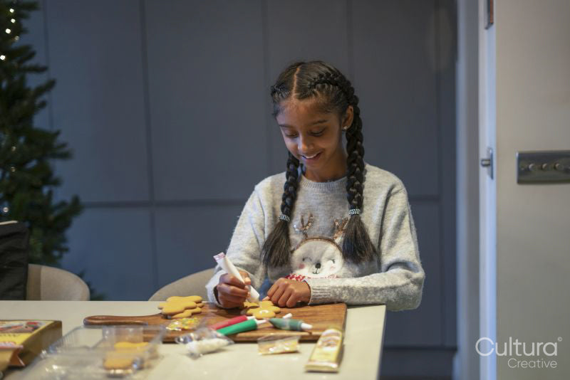 Smiling girl decorating gingerbread cookies in kitchen