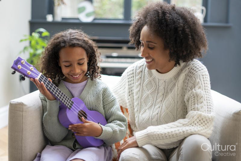 Mother assisting daughter playing ukulele at home