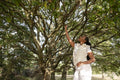 Young woman standing under tree, reaching to branch
