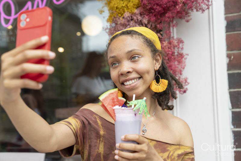 Young woman taking selfie while drinking smoothie in front of cafe