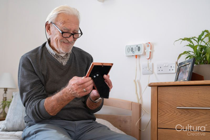 Smiling senior man sitting on bed and looking at photography