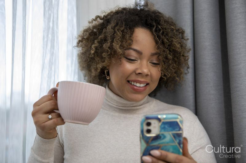 Smiling woman holding coffee cup and looking at smart phone