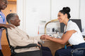 Smiling female doctor talking to senior woman sitting in wheelchair in doctors office