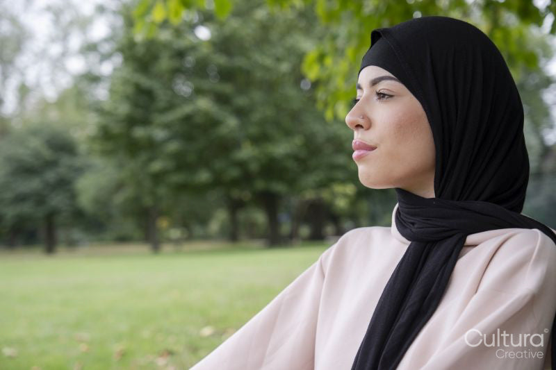 Portrait of woman in hijab and pink tracksuit meditating in park