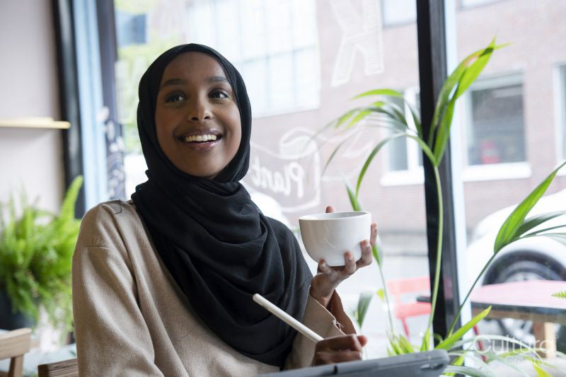 Smiling young woman in hijab drinking coffee in cafe