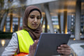 Female engineer in hijab and hardhat using digital tablet