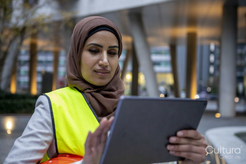 Female engineer in hijab and hardhat using digital tablet