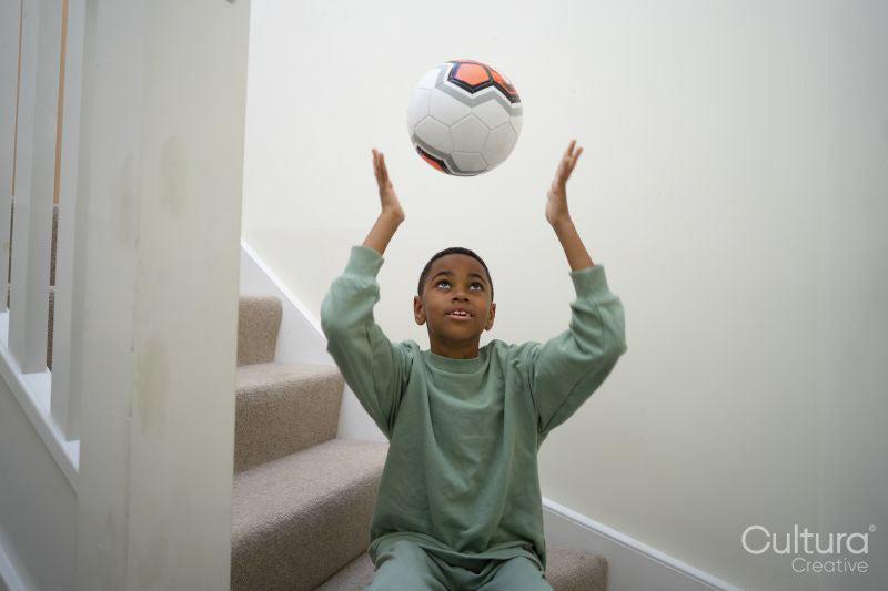 Boy sitting on stairs and throwing soccer ball in air