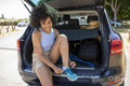 Young woman sitting at back of car putting on hiking shoes