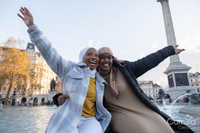 Smiling young female tourists in hijabs hugging in city square