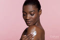 Young woman applying cream on shoulder