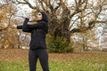 Woman in black sports clothing and hijab stretching in park