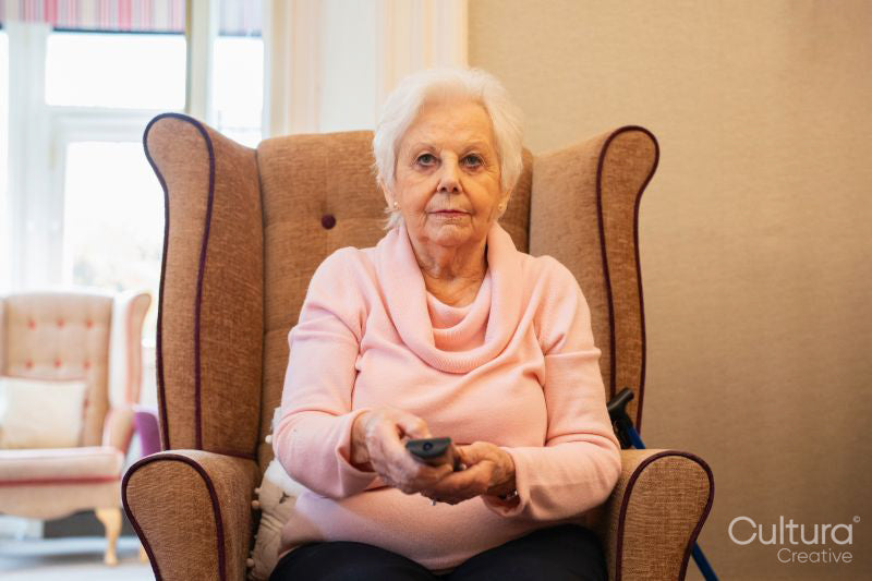 Senior woman sitting in armchair and using remote control