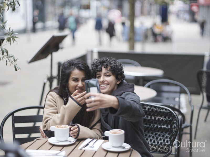 Smiling female couple taking selfie in sidewalk cafe