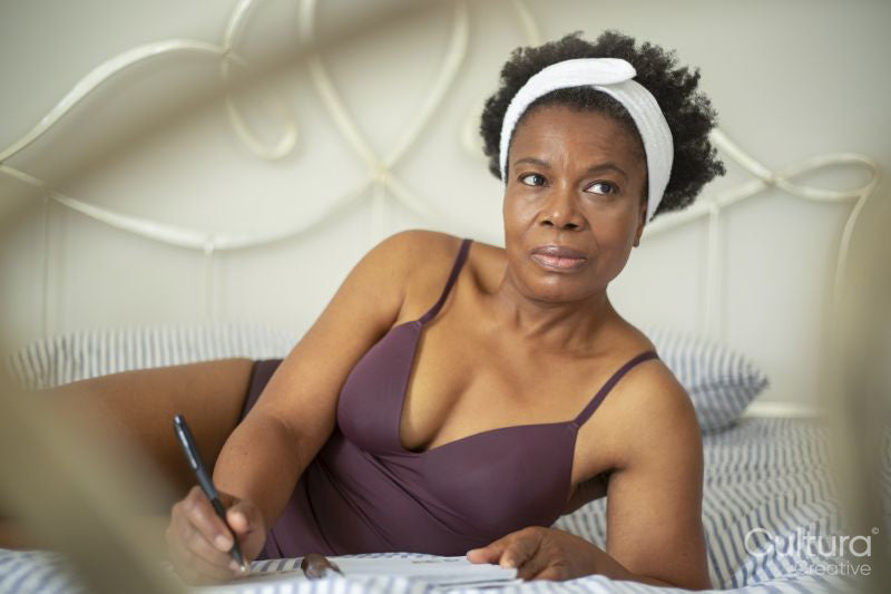 Woman in lingerie writing in notebook on bed