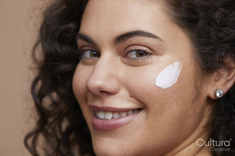 Close-up portrait of young woman applying face cream
