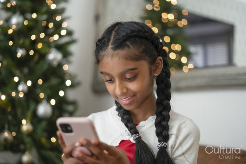 Smiling girl looking at smart phone at Christmas tree