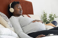 Pregnant woman with headphones relaxing on bed
