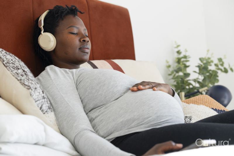 Pregnant woman with headphones relaxing on bed