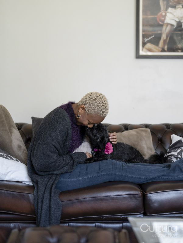 Woman stroking dog on sofa at home