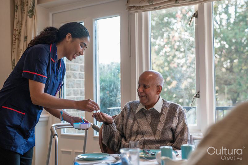 Nurse giving pill to senior man during dinner at cafeteria in nursing home