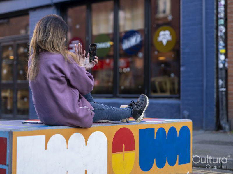 Woman taking selfie while sitting on wall in city