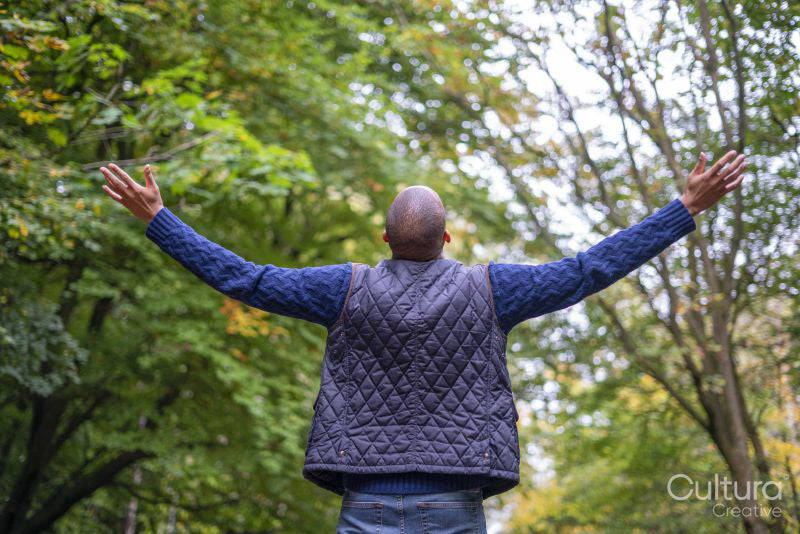 Back View of man standing in forest with outstretched arms