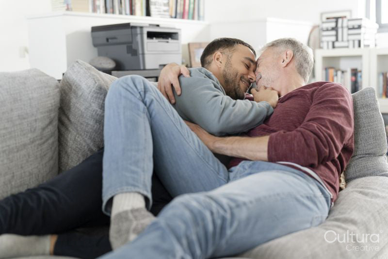 Smiling male couple cuddling on sofa at home